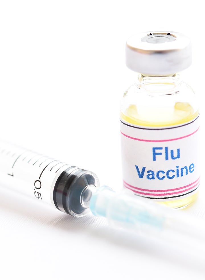 A syringe is sitting next to a bottle of flu vaccine