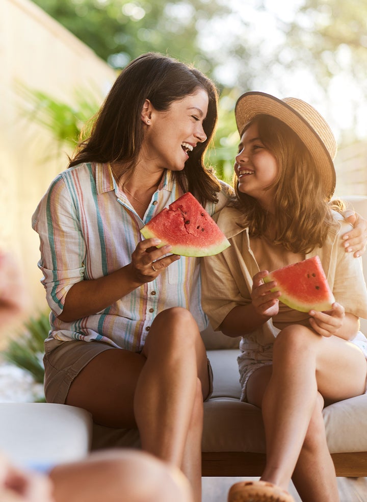 Two women are sitting on a couch eating watermelon