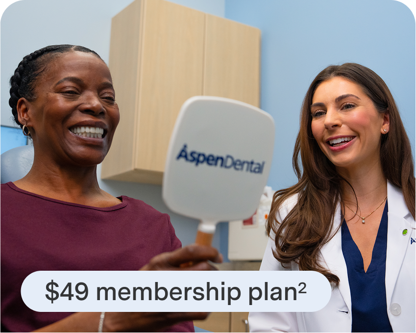 Smiling patient admiring her teeth in an Aspen Dental mirror while talking with a friendly dental professional, showing the $49 membership plan.
