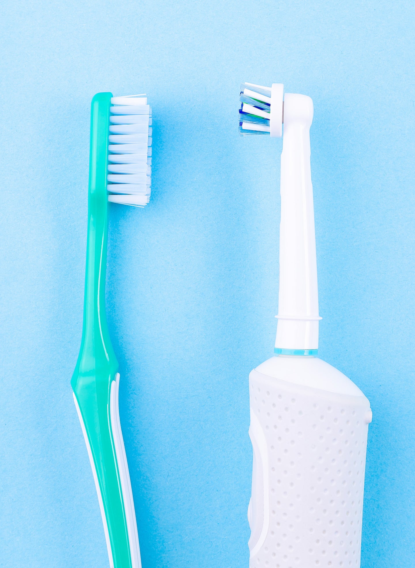 A manual toothbrush with a green handle and white bristles next to a white electric toothbrush with a detachable brush head on a light blue background.