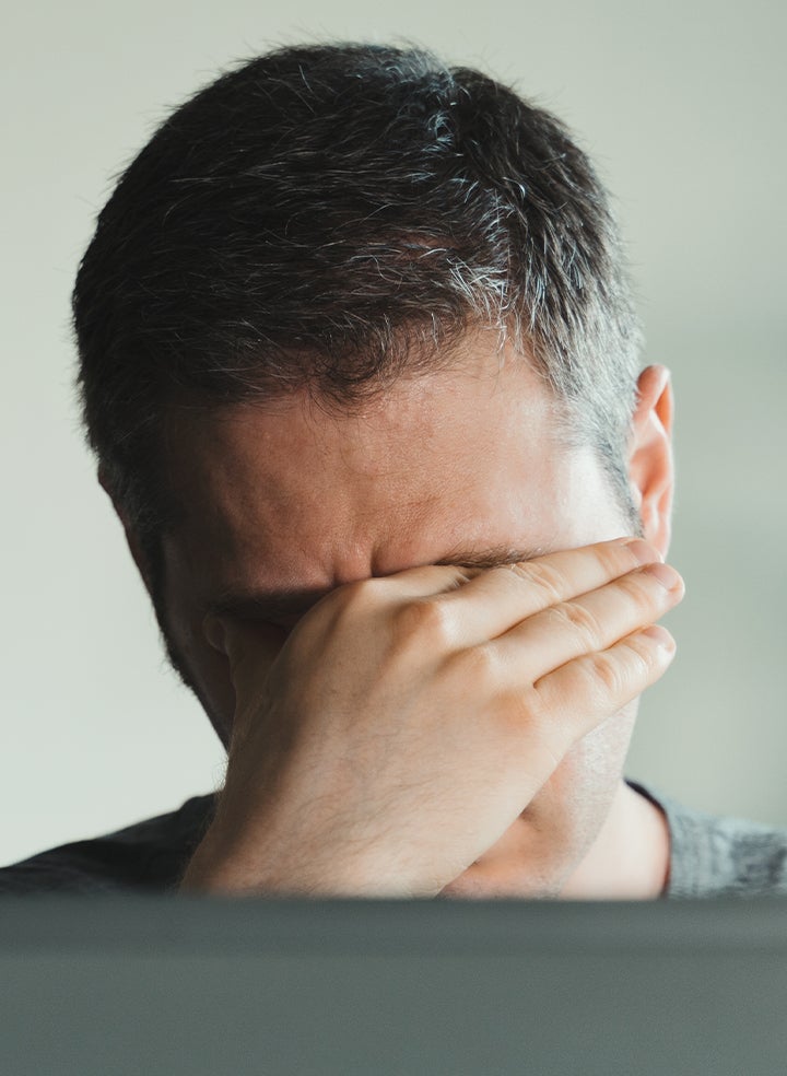 A man is rubbing his eyes in front of a laptop