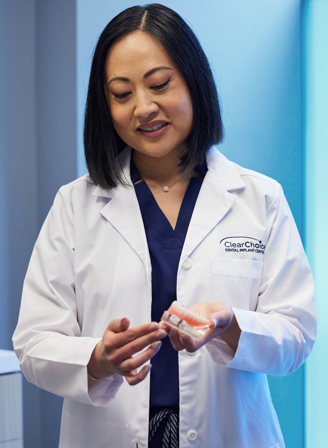 A female ClearChoice doctor smiling in a lab coat holding a pair of dentures explaining the MRI process with dental implants to a patient. 