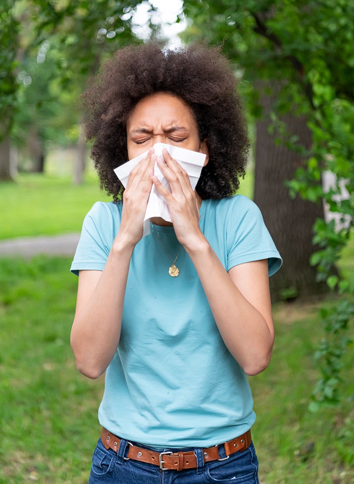 A woman is blowing her nose into a tissue in a park