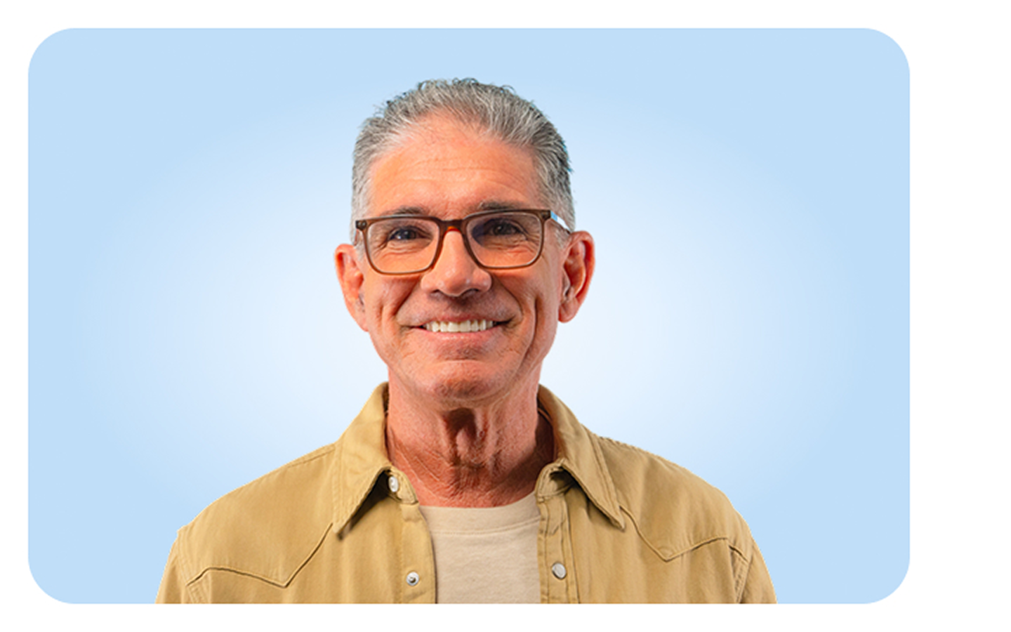 A man wearing glasses and a tan shirt smiles for the camera