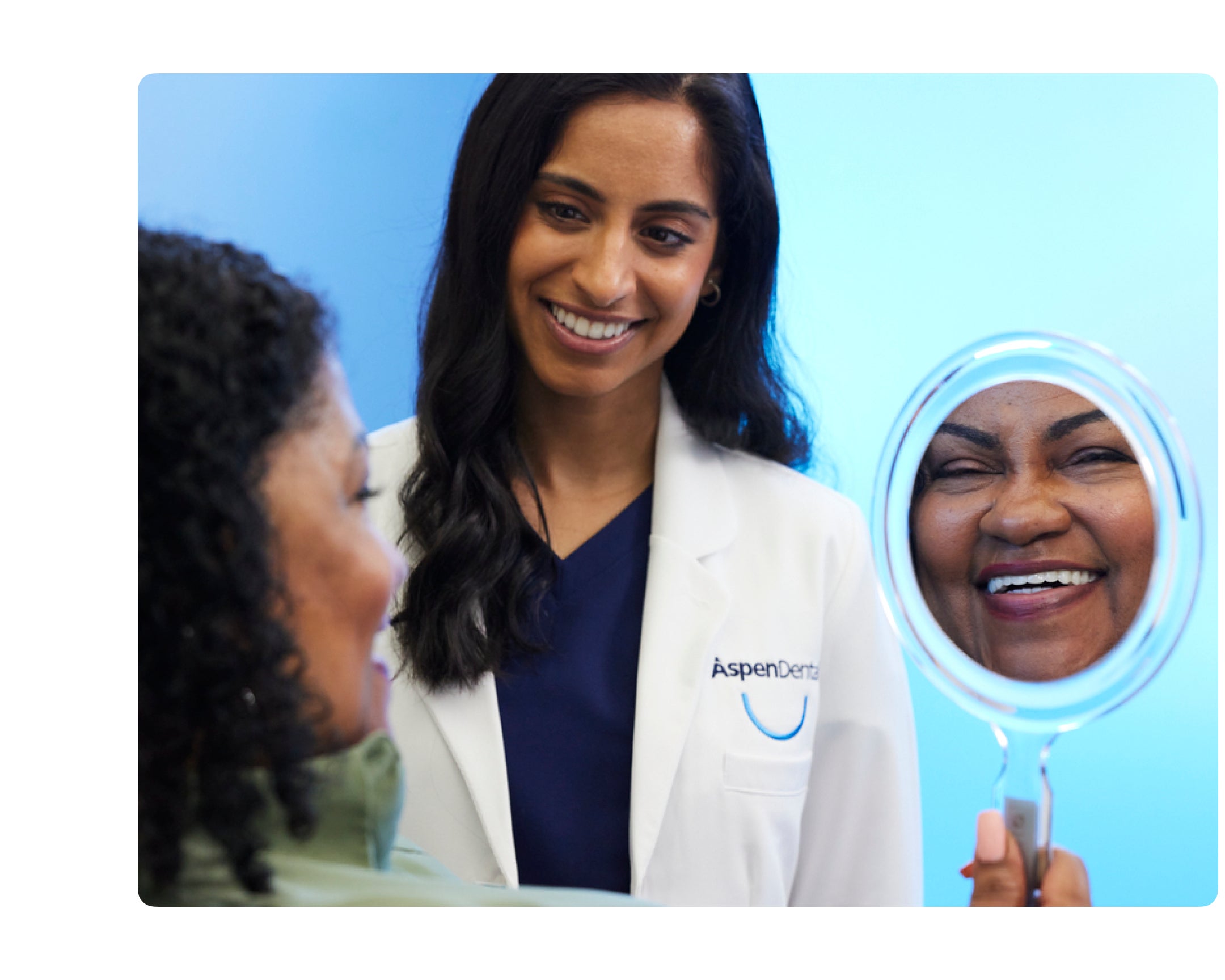 A woman in a lab coat looks at a patient's smile in a mirror