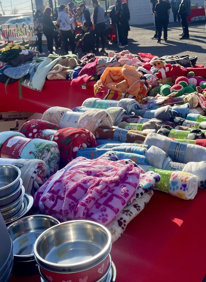 A table with a red tablecloth covered in piles of colorful blankets and pet toys.