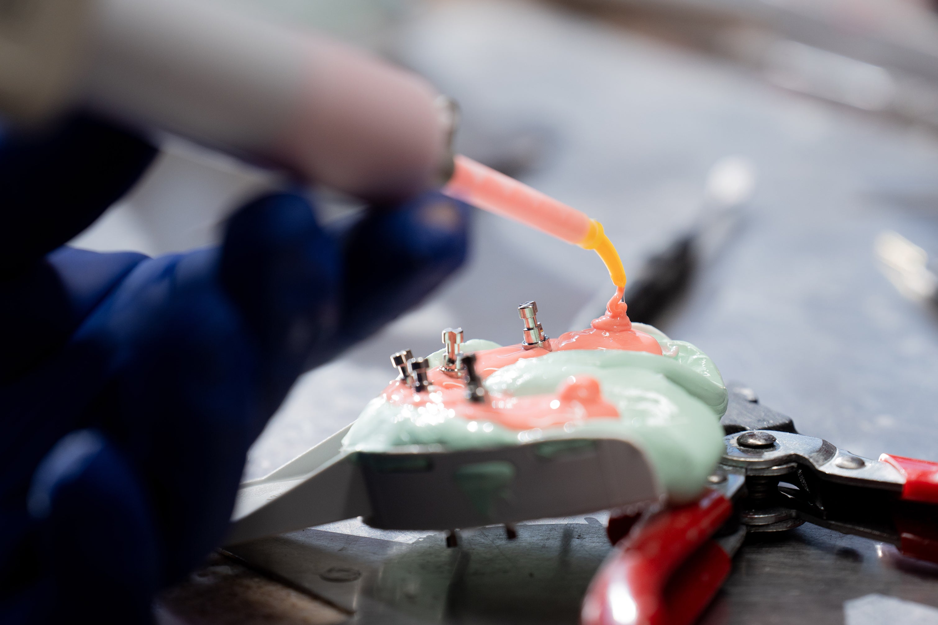 Close-up of a dental technician applying material to a dental implant model with visible metal abutments, showing how dental implants are made and assembled.