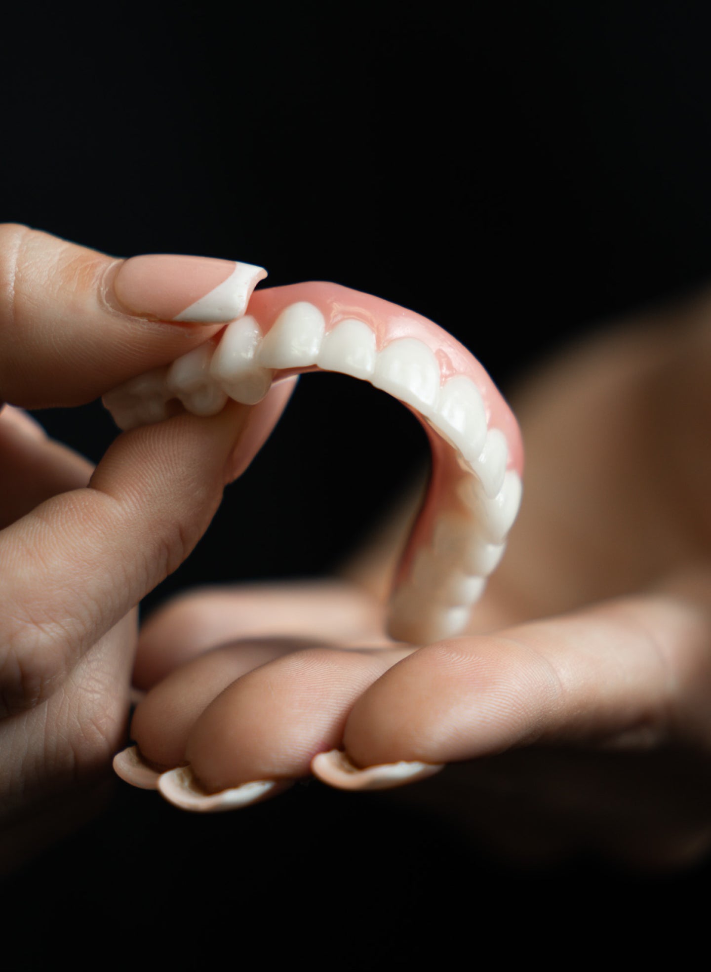 Close-up view of a flexible denture held gently by a hand, showcasing realistic teeth and gum design against a dark background.