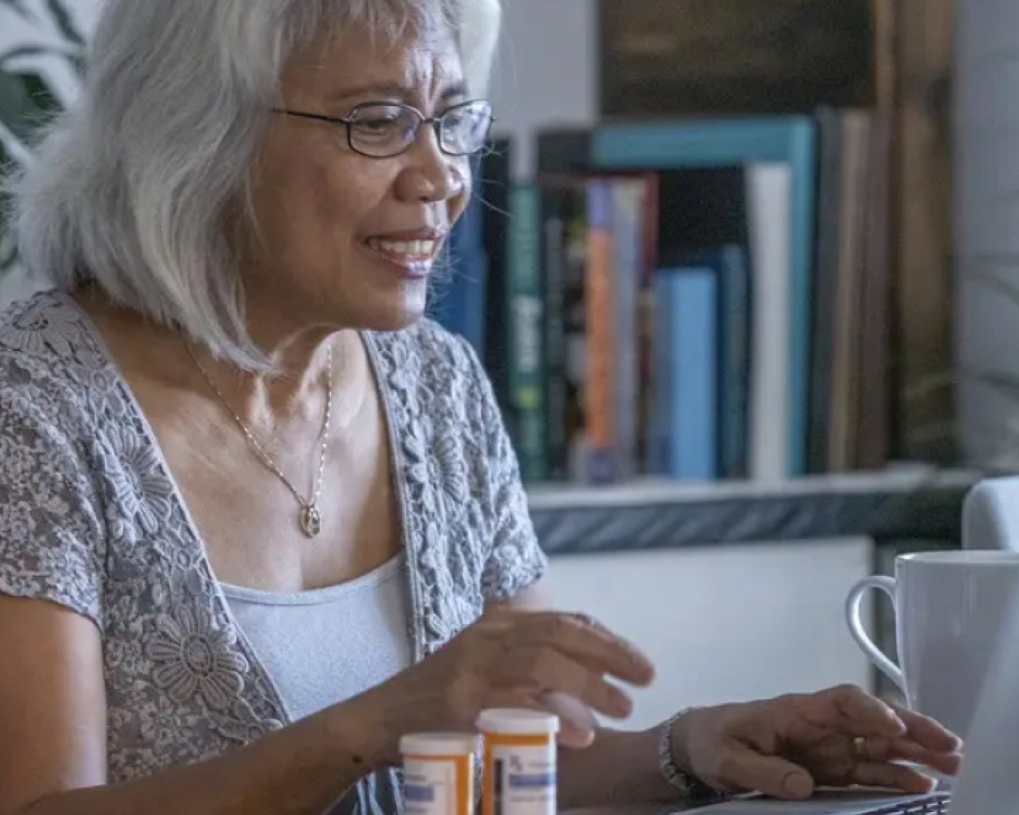 A woman sitting at a table with her medication, she is chatting to a medical provider via a virtual care call.
