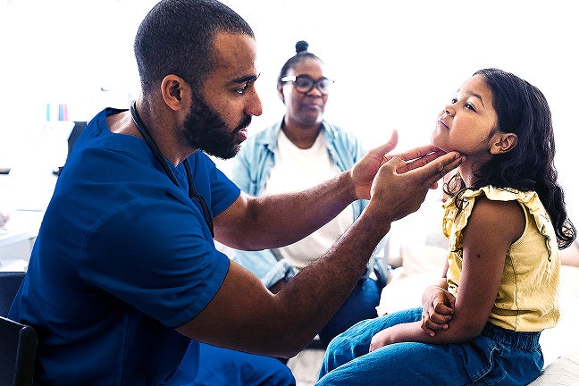 Doctor giving a child a checkup with a parent watching in the background.