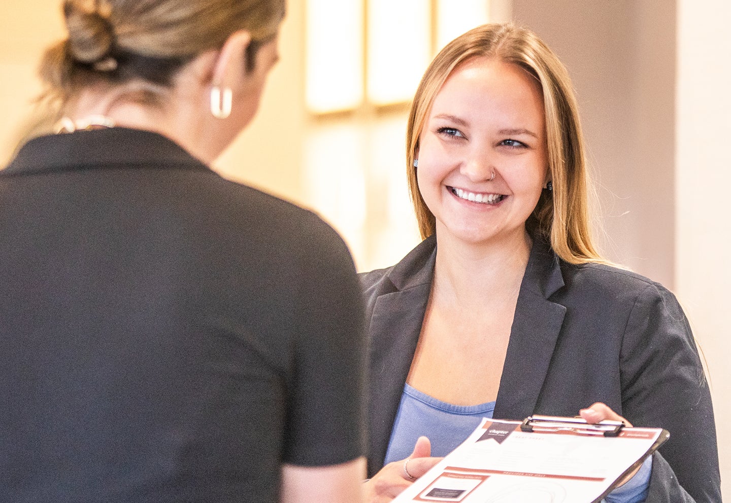 A woman smiles, handing over a chapter rewards clue membership sign up sheet to a guest