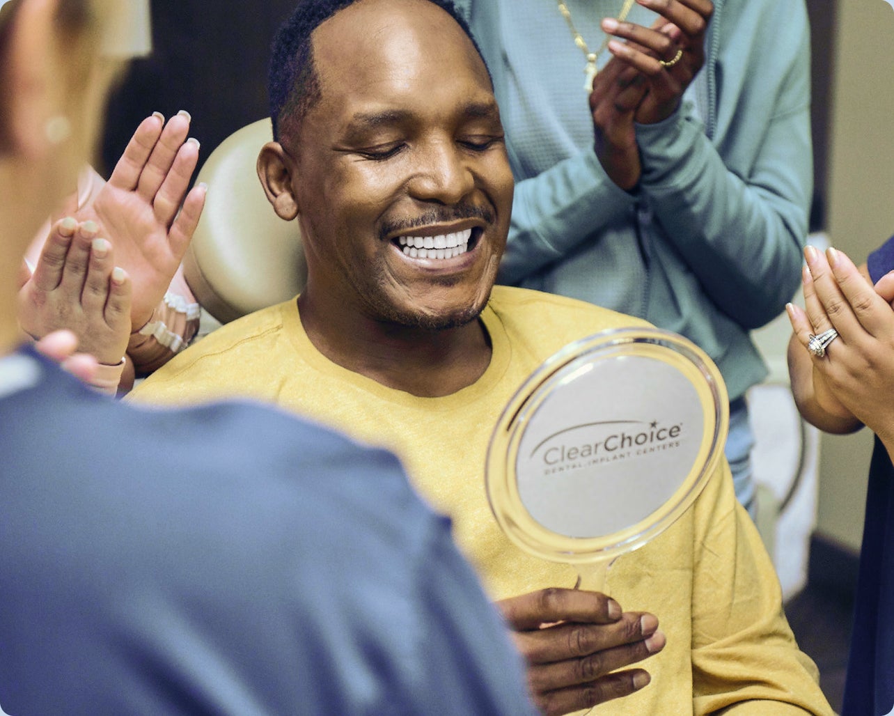 A patient wearing a yellow shirt sitting in a clinic, surrounded by ClearChoice doctors celebrating his new Endura Elite dental implants.
