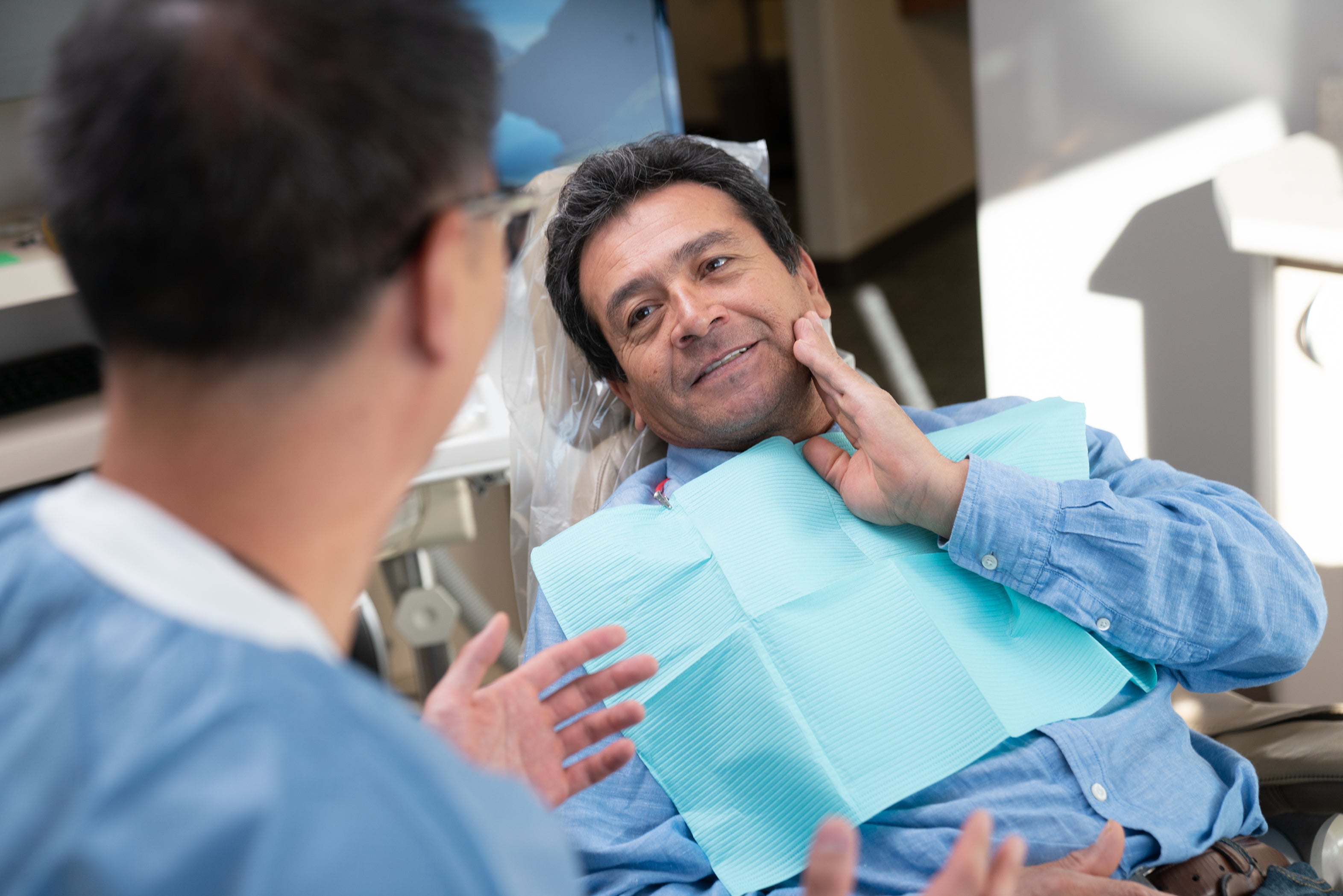 Man touches cheek while talking to dentist, showing concern about swelling after dental implants.