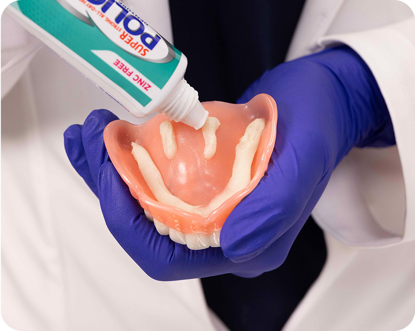 Applying denture adhesive paste in short strips onto an upper denture – Aspen Dental how-to guide.
