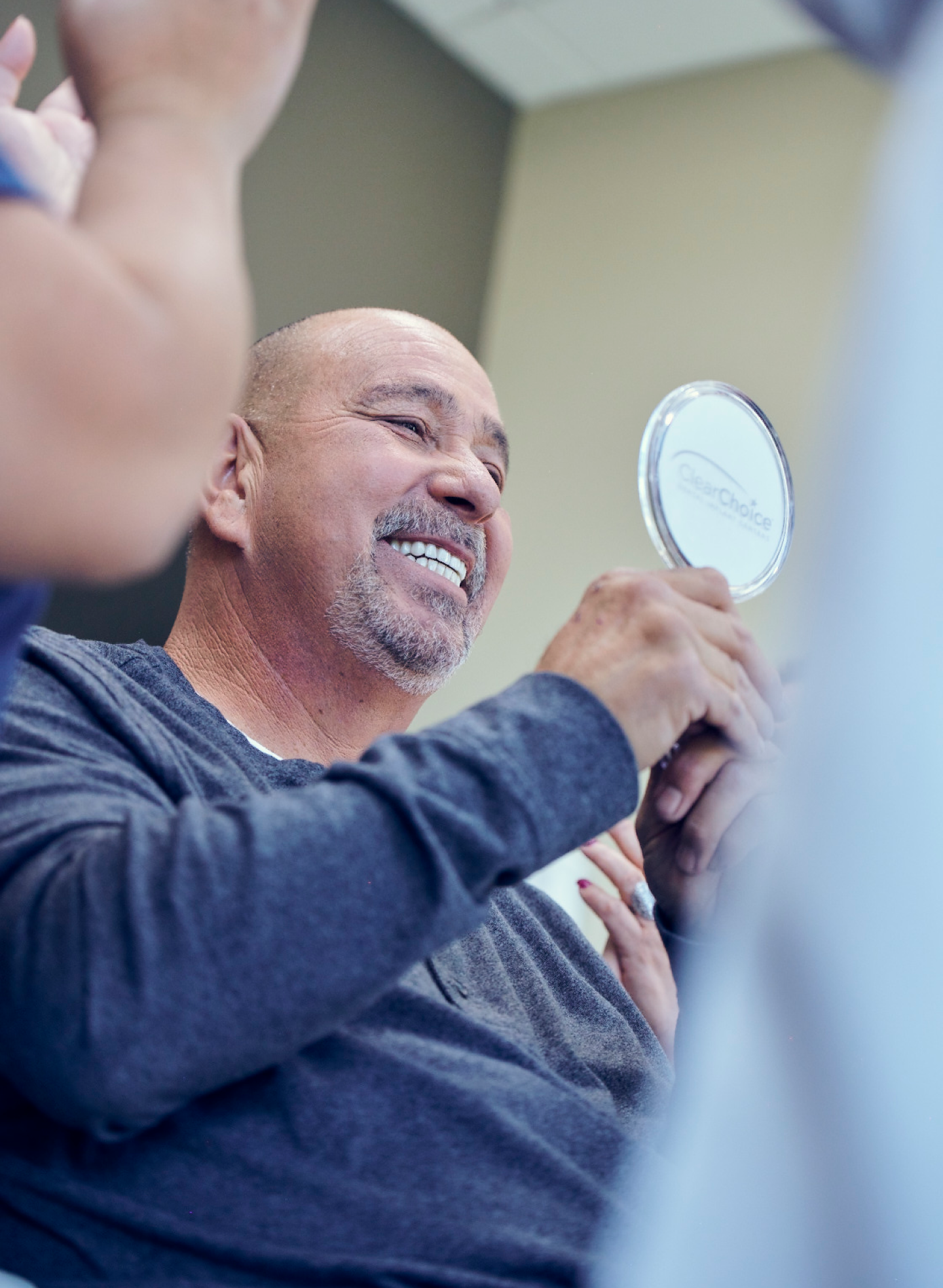 Happy man holding a mirror and smiling, reflecting satisfaction with his dental restoration options, showcasing the benefits of dental implants versus crowns with ClearChoice.