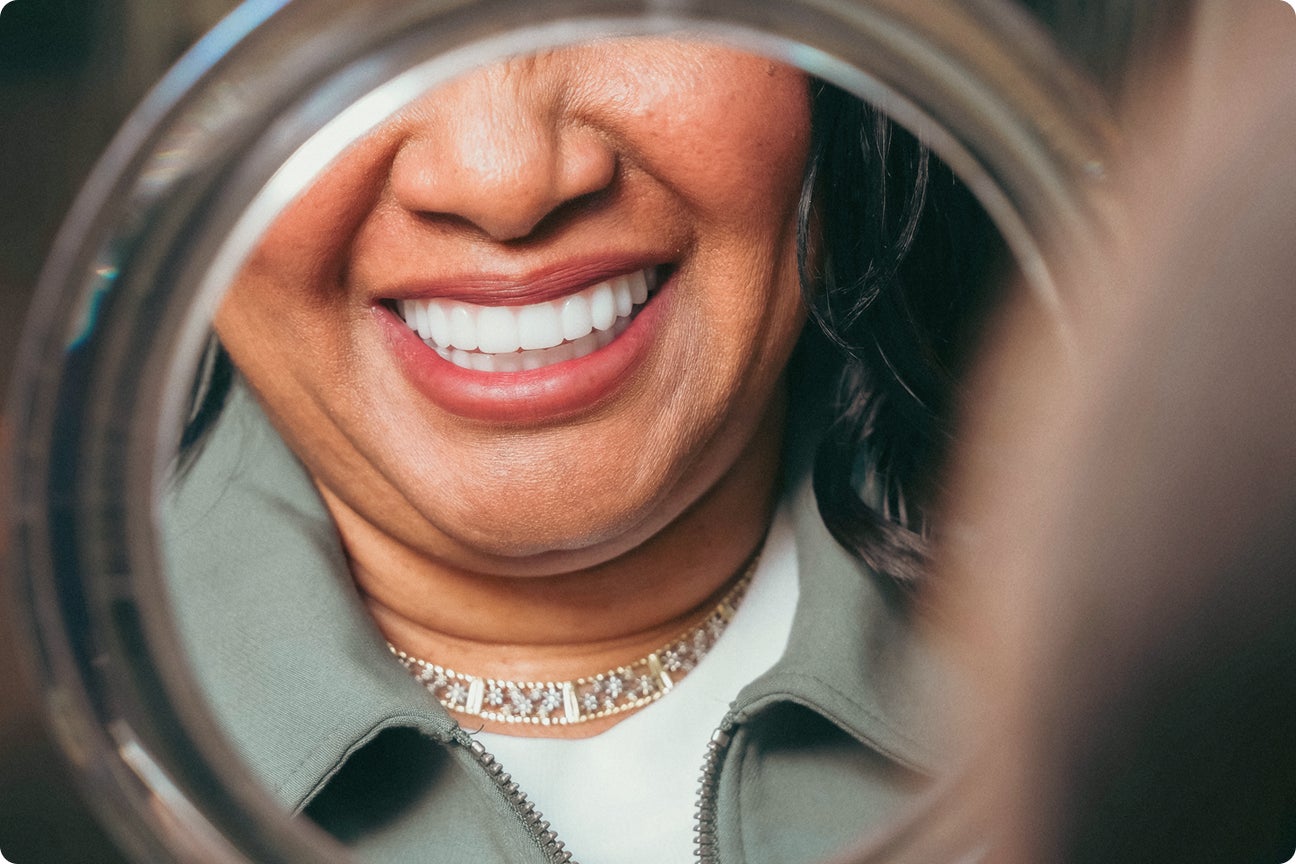 An image of a ClearChoice patient smiling into a mirror after her full mouth restoration treatment.