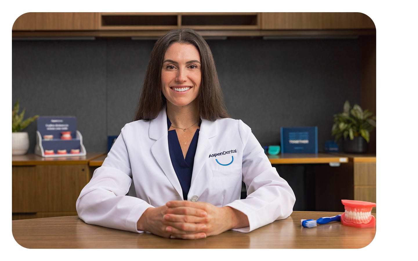 Aspen Dental provider seated at desk with denture model and toothbrush for patient care education