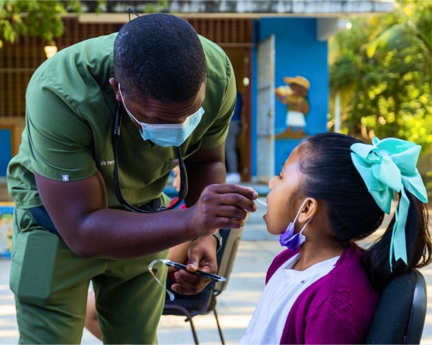 A uniformed Aspen Dental professional providing dental care to a smiling child outdoors during the Healthy Mouth Movement event.