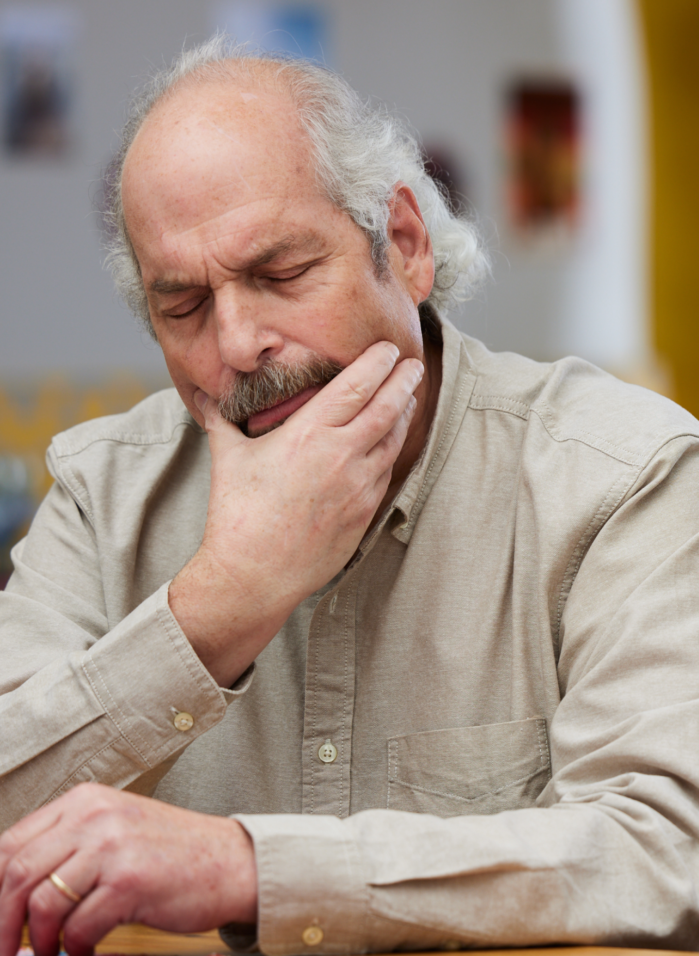 An elderly man with a thoughtful expression, resting his hand on his chin, appears concerned. He is considering dental implants, reflecting common concerns of ClearChoice patients exploring implant solutions for tooth replacement.
