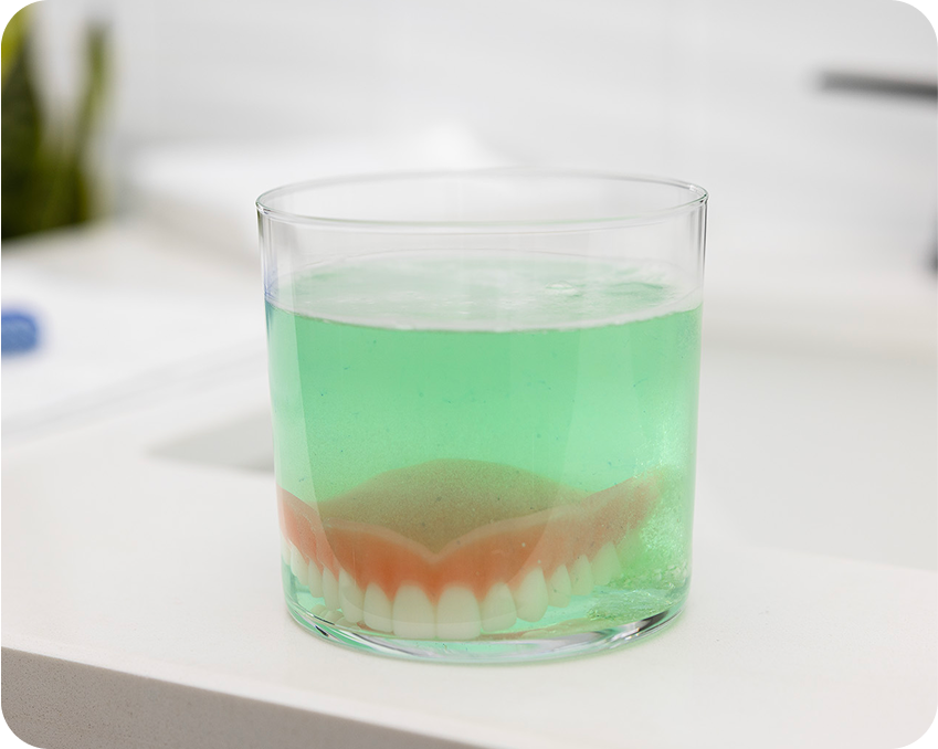  Upper denture soaking in green cleaning solution after removal – Aspen Dental hygiene step.