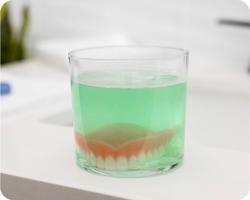 Upper denture soaking in green cleaning solution after removal – Aspen Dental hygiene step.