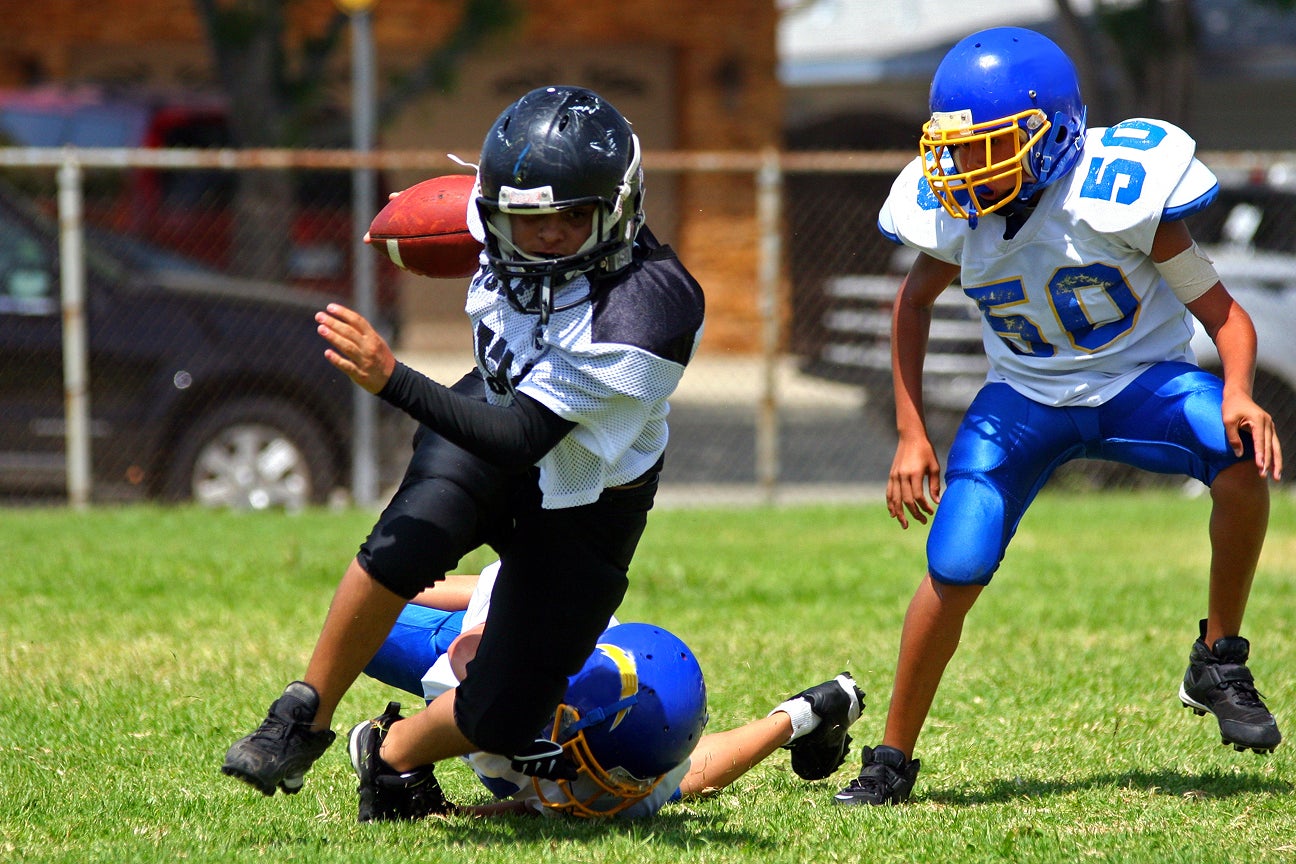 Three children wearing football gear and playing football.