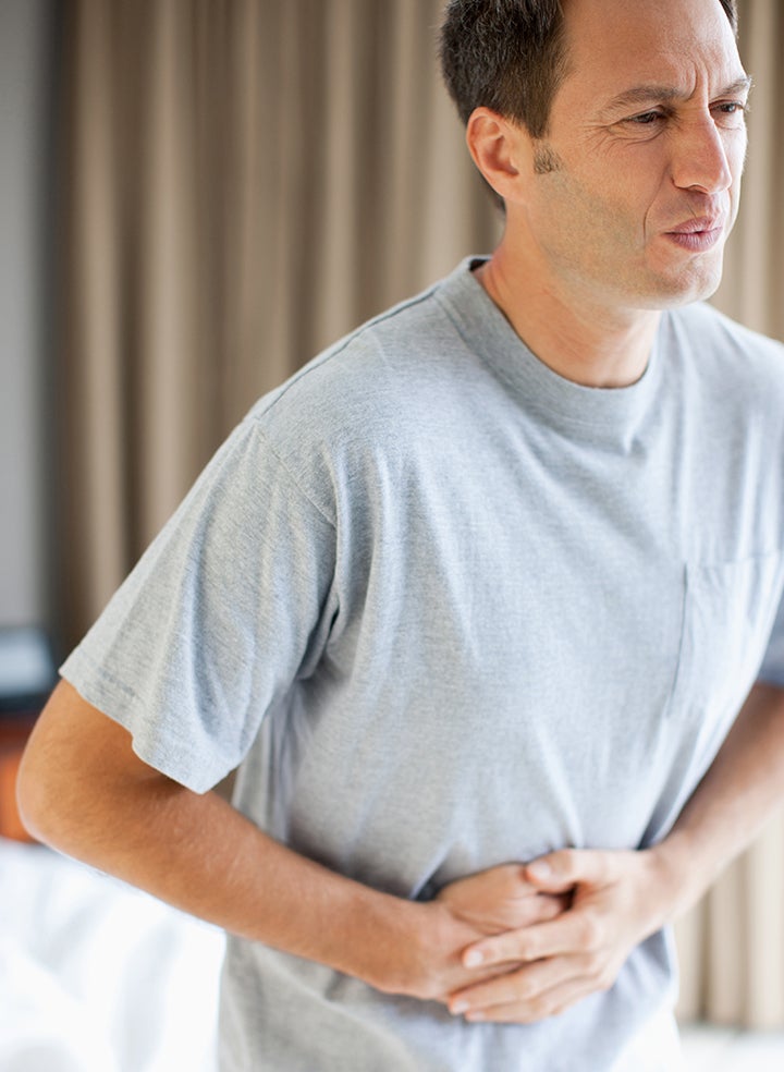 A man in a grey shirt is holding his stomach in pain