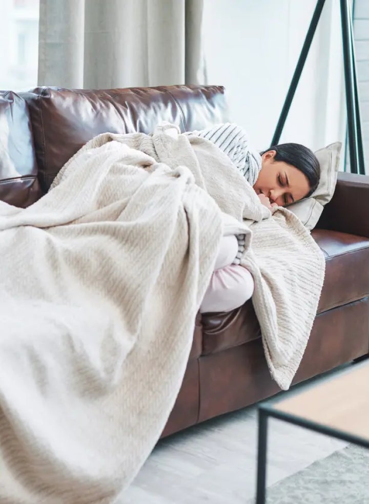 A woman is sleeping on a couch under a blanket.