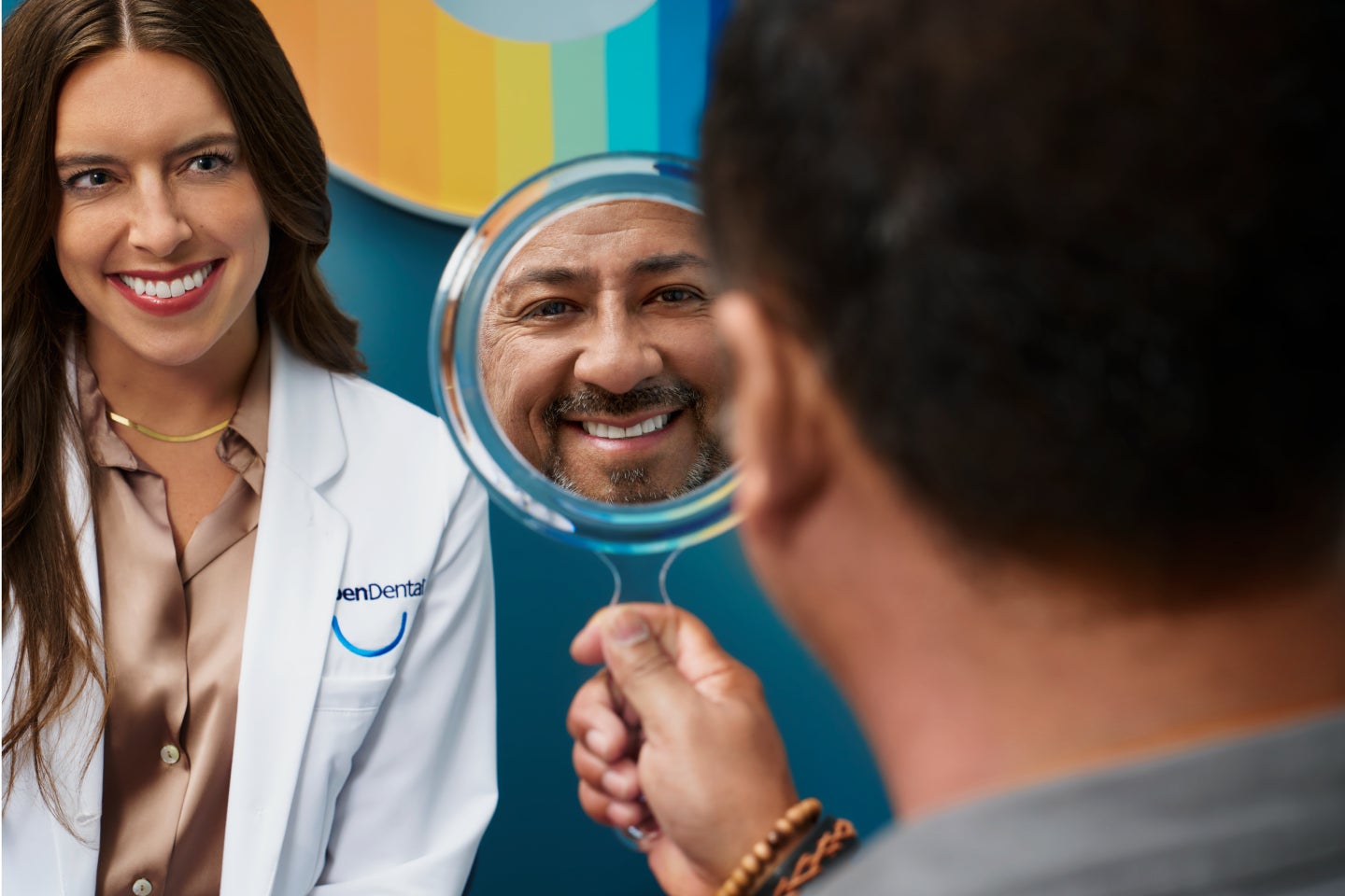 Smiling person holding Motto clear retainer close to the camera, showcasing its transparent design in a professional dental setting.