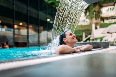Person relaxing in an outdoor thermal pool with waterfall at Thermes de Spa, nestled in woodland near Spa, Belgium
