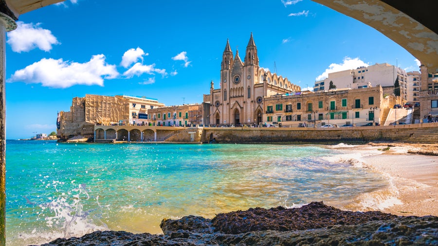 Saint Julian's beach in Malta with historic buildings in the background, including the iconic Balluta Buildings overlooking Balluta Bay