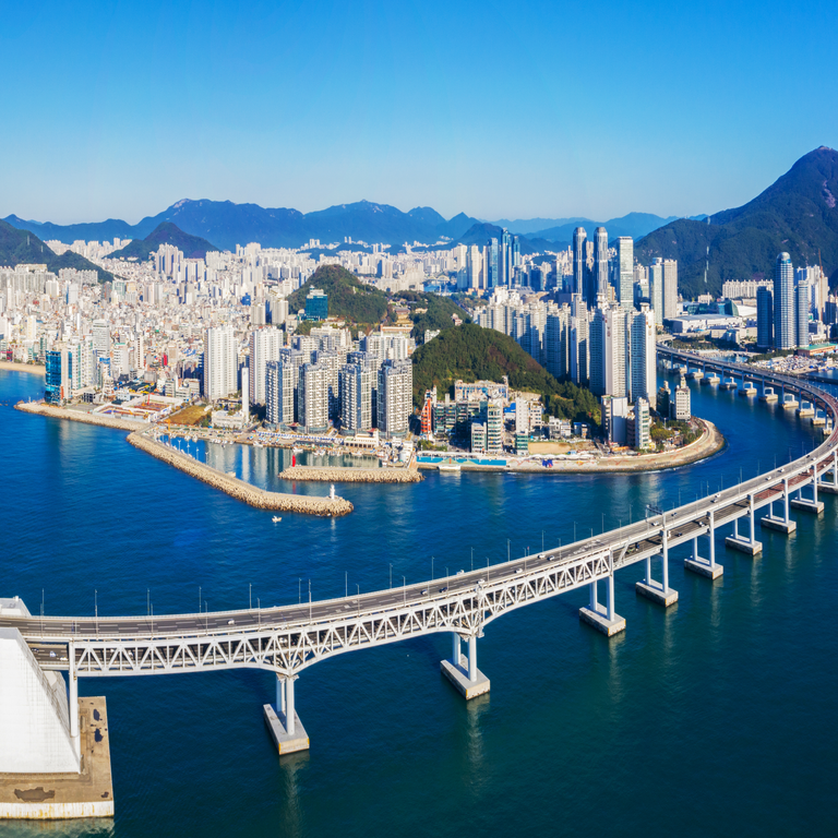 Cityscape of Busan, South Korea with modern skyscrapers, Gwangan Bridge, coastline, and surrounding green hills
