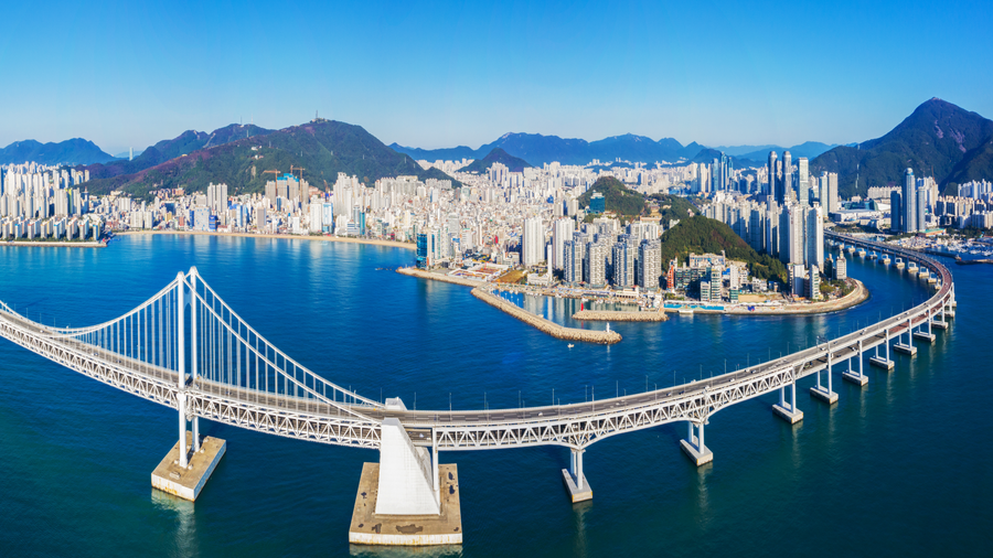 Cityscape of Busan, South Korea with modern skyscrapers, Gwangan Bridge, coastline, and surrounding green hills