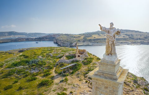 Statue of Saint Paul in St. Paul’s Bay, Malta, depicting the saint holding a staff and book against a coastal backdrop