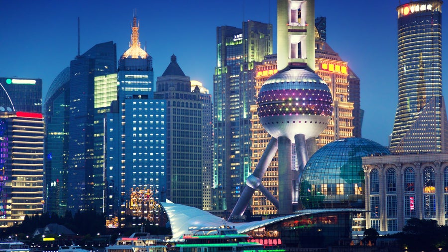 Aerial view of urban landscape with towering skyscrapers, modern shopping complexes, and Huangpu River at night in Shanghai, China