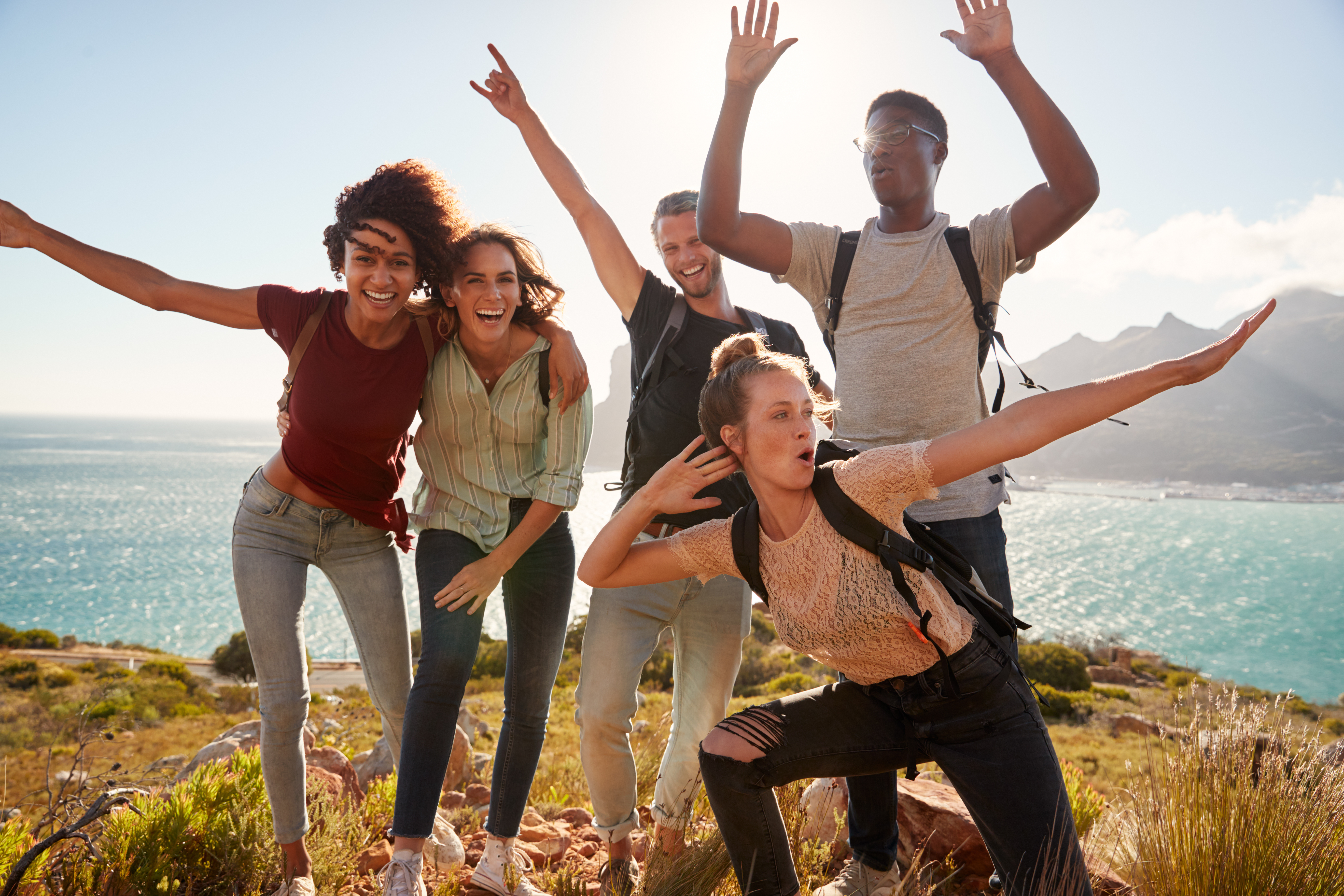 Millennial friends celebrating on a hiking trip after reaching the summit, posing for photos
