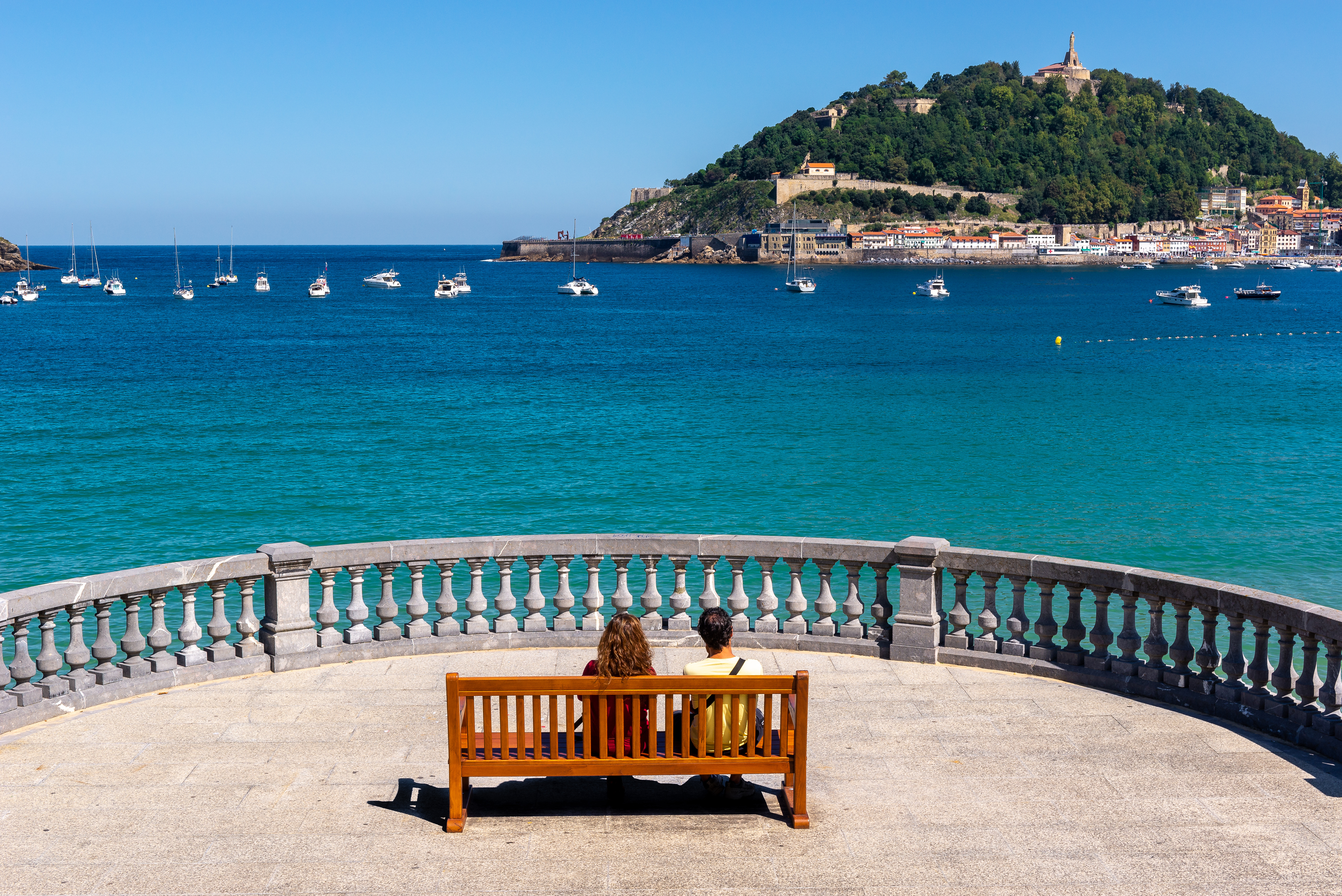 Tourists sitting on a bench overlooking the beach in San Sebastián, Spain, enjoying the seaside view