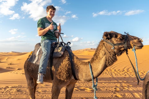 Tourist riding a camel in the nearby Agafay Desert outside Rabat, Morocco, with sandy dunes in the background