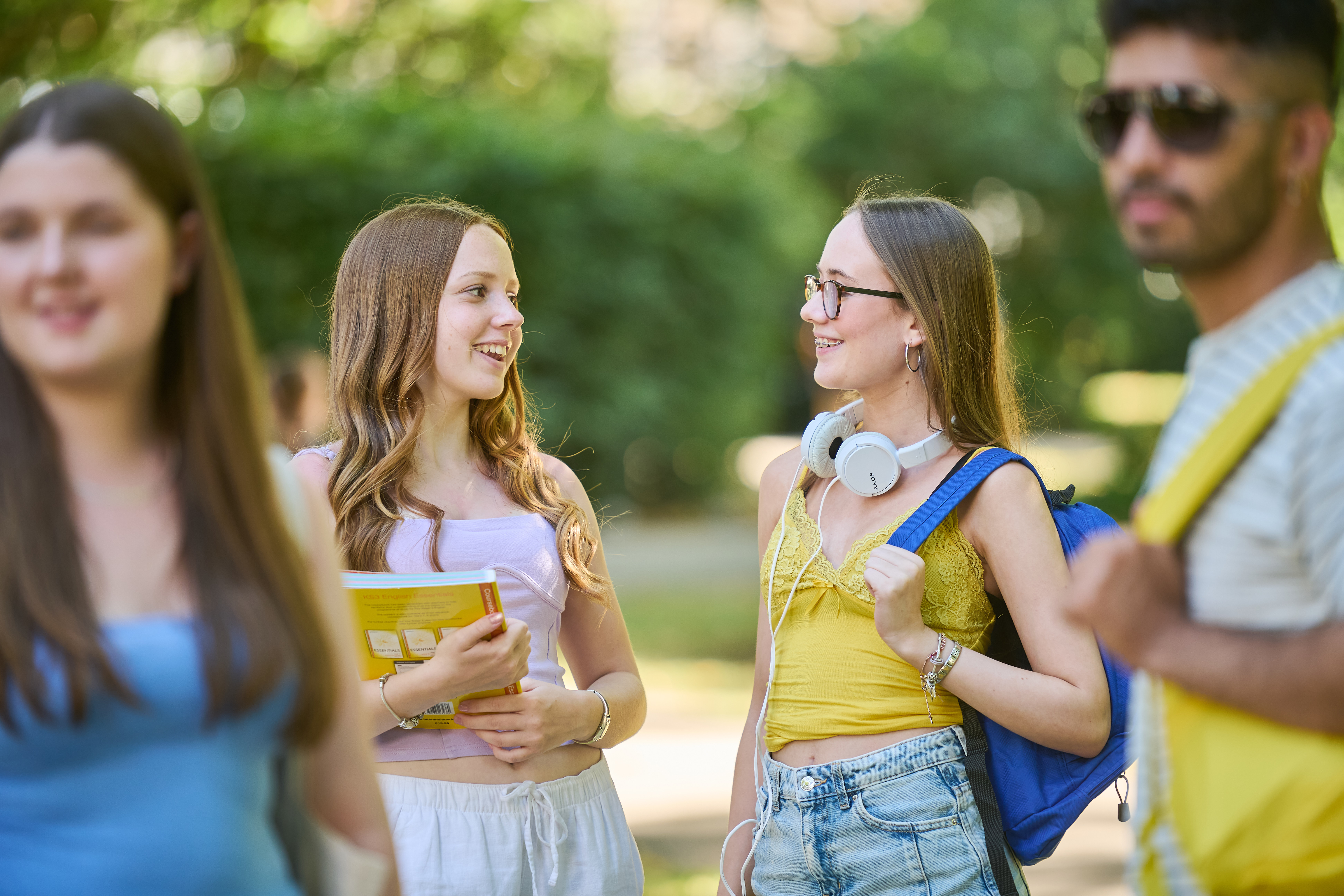 ESL teen students walking in a London park with backpacks and folders talking