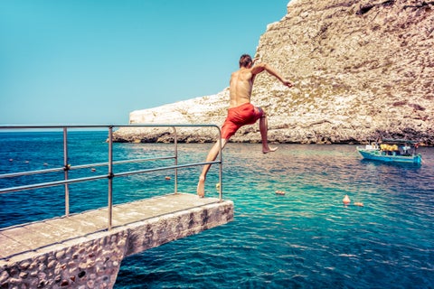 Tourist jumping into the clear blue sea from rocky cliffs in Gozo, Malta