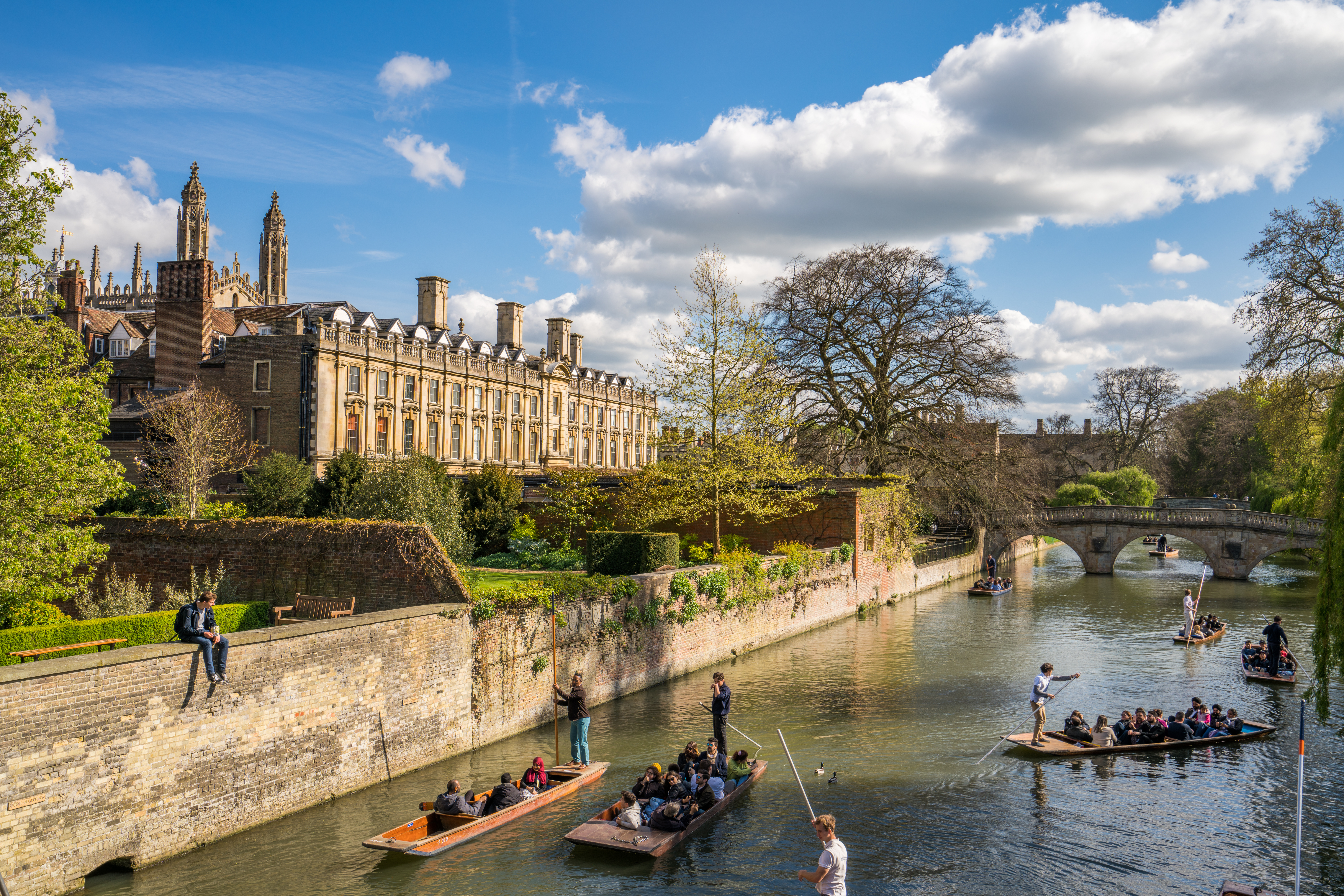 Tourist boats on the River Cam with historic bridge and college building, Cambridge UK
