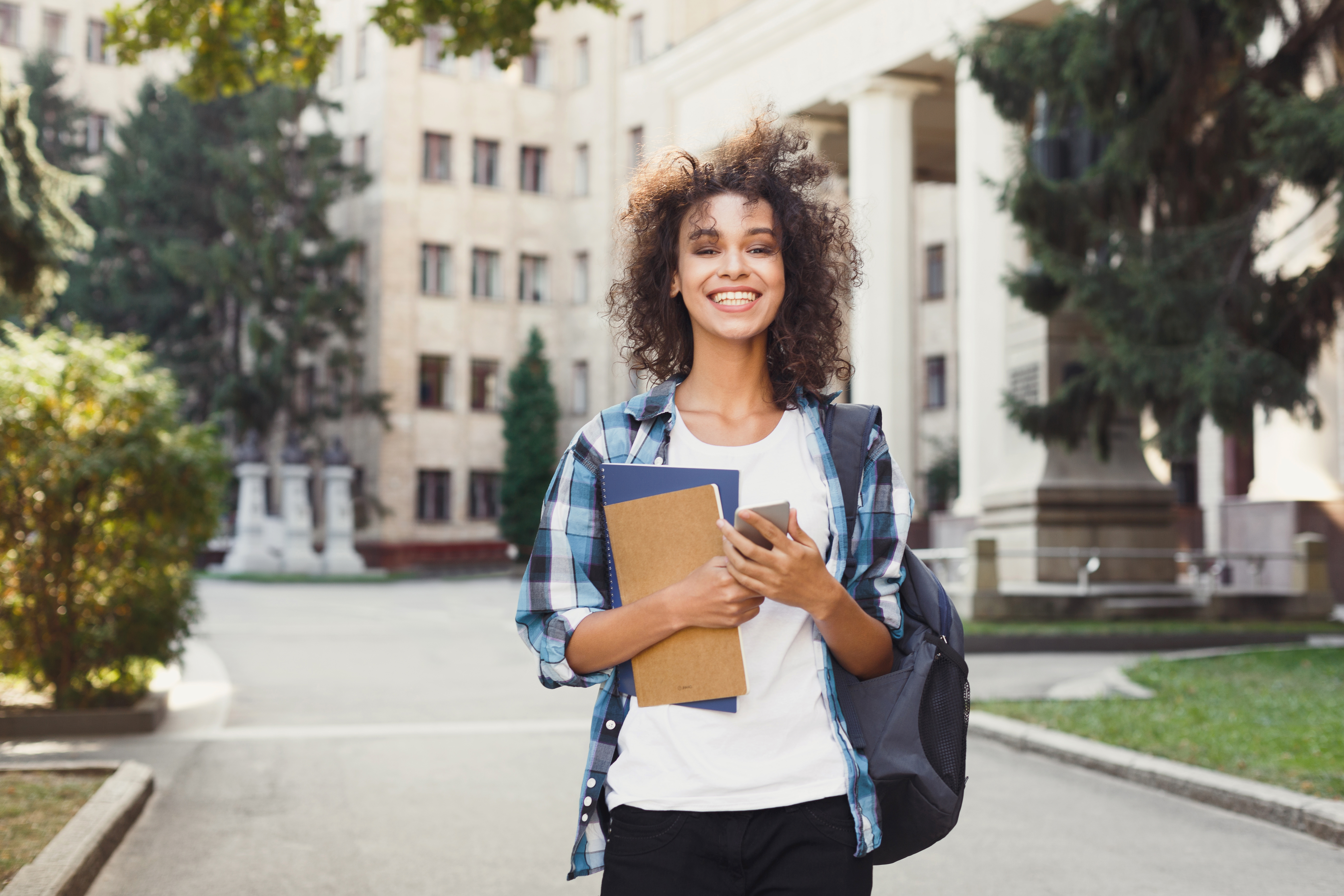 Smiling student posing with books outside university campus