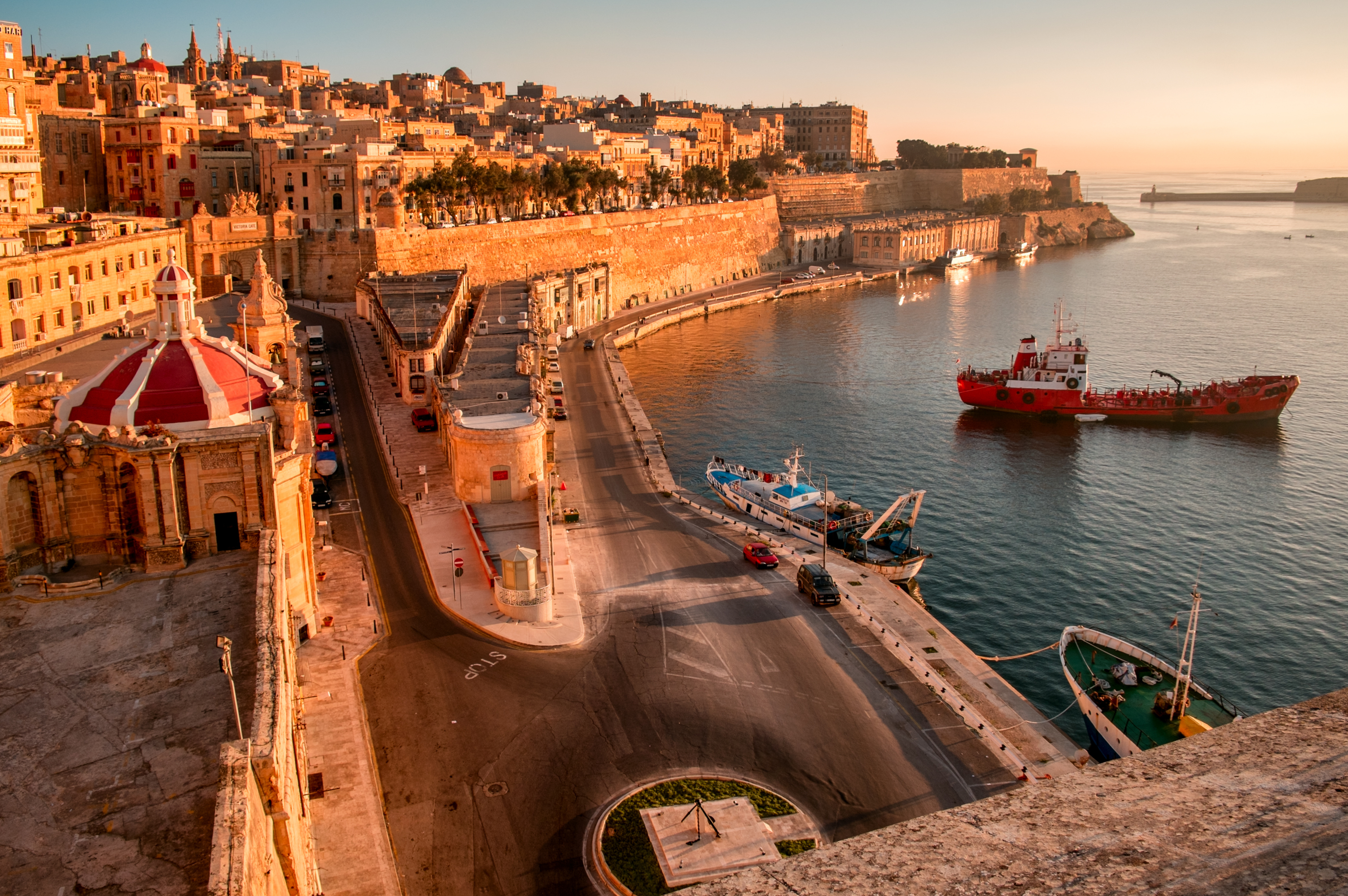 Colorful Maltese Luzzu boats with eyes of Osiris in Balluta Bay, St. Julian’s, Malta, surrounded by historic buildings, modern apartments, and a prominent church steeple