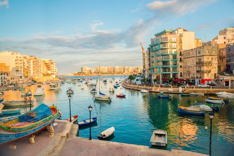 St. Julian's waterfront in Malta with boats anchored in the calm sea and coastal buildings lining the shore