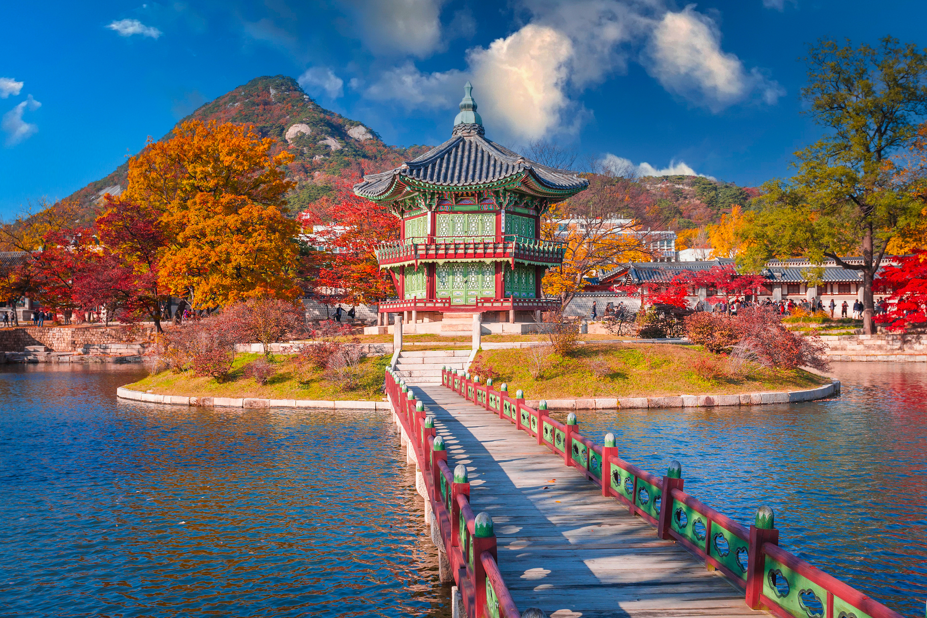 Gyeongbokgung Palace in Seoul, South Korea, during autumn with colorful foliage, a calm lake, and blue sky
