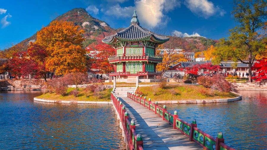 Gyeongbokgung Palace in Seoul, South Korea, during autumn with colorful foliage, a calm lake, and blue sky