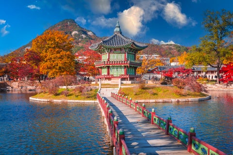 Gyeongbokgung Palace in Seoul, South Korea, during autumn with colorful foliage, a calm lake, and blue sky