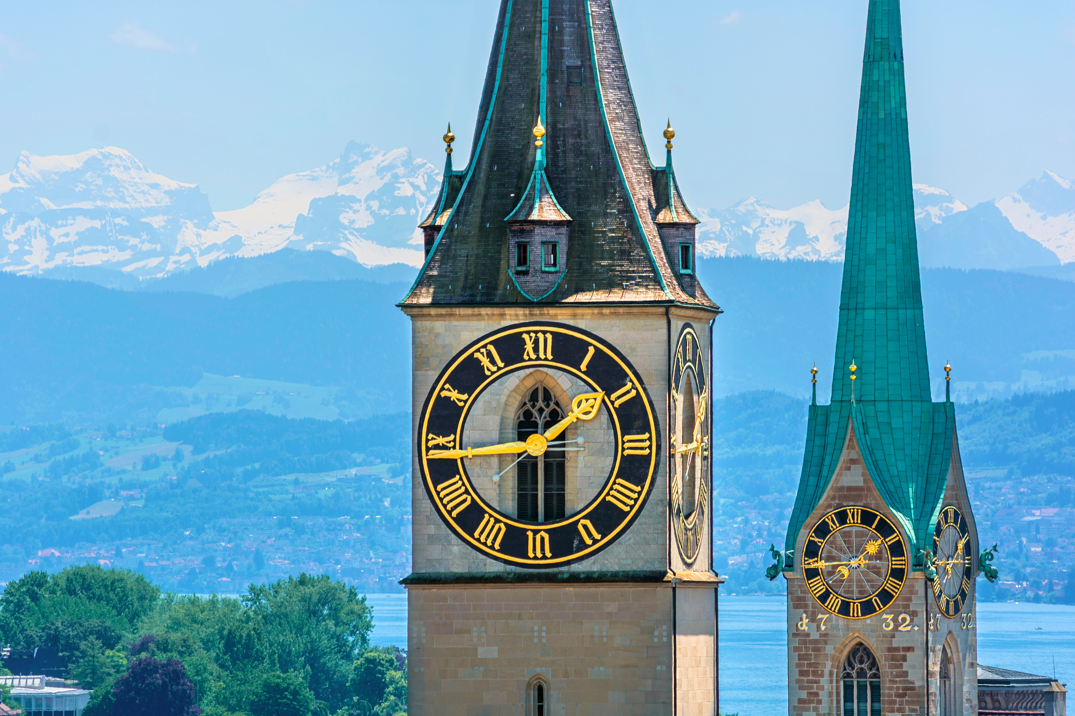 St. Peter’s Church clock tower in Zurich, Switzerland, with the Uetliberg mountain and Swiss Alps visible in the background