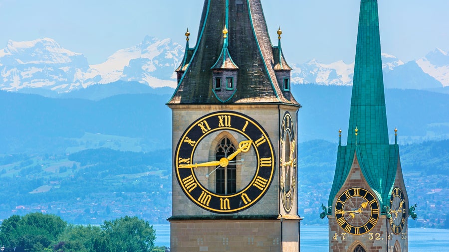 St. Peter’s Church clock tower in Zurich, Switzerland, with the Uetliberg mountain and Swiss Alps visible in the background