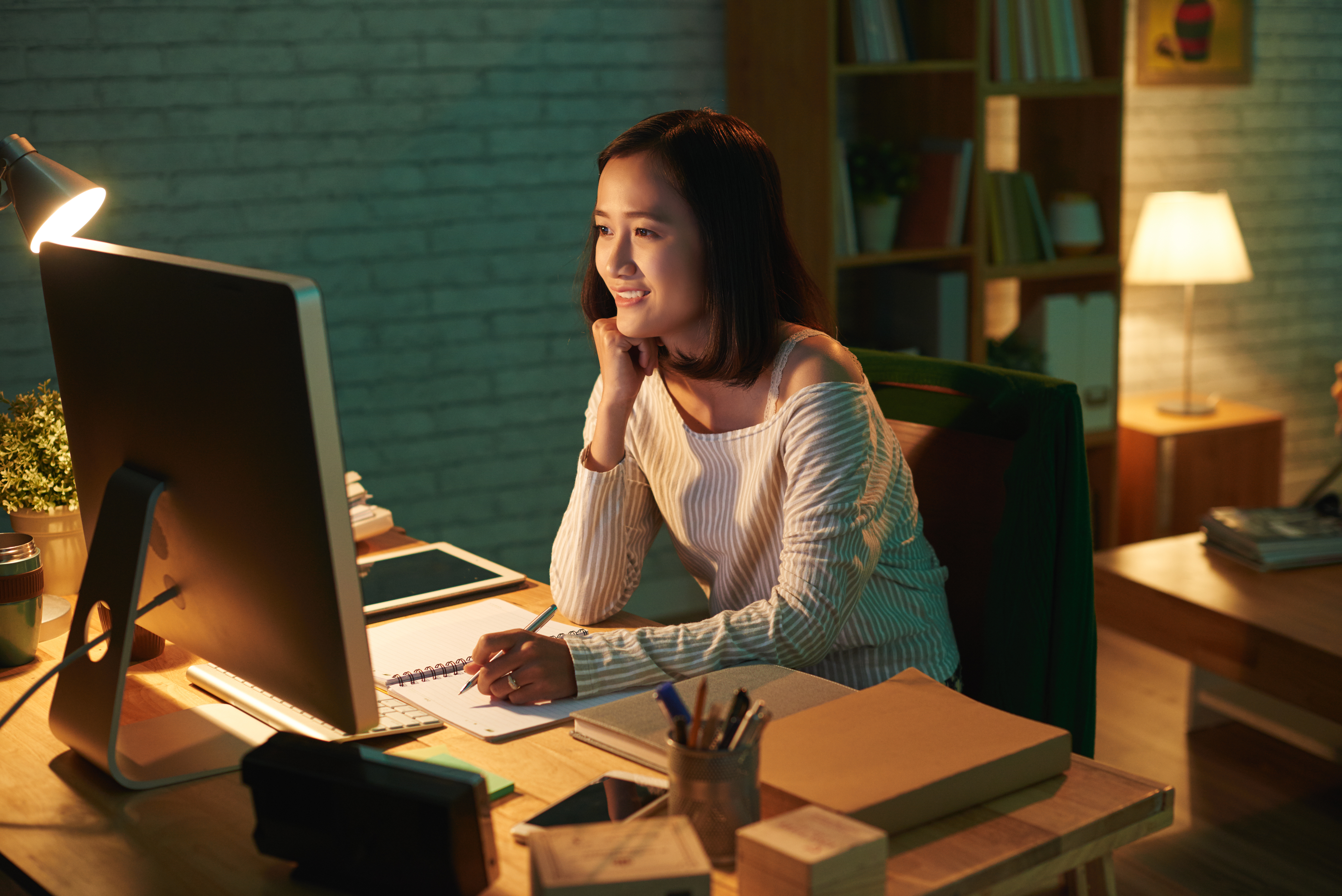 Woman sitting at a desk using computer attending remote classes in a bright, beautiful living room